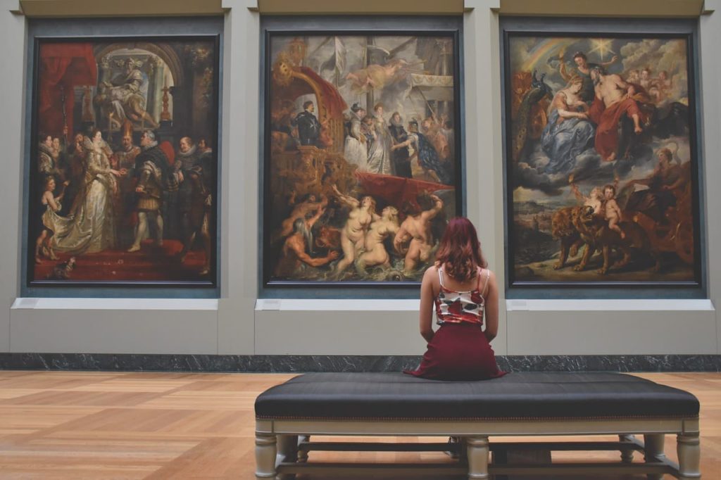a woman sitting on a bench in front of large works of art in an Italian art gallery